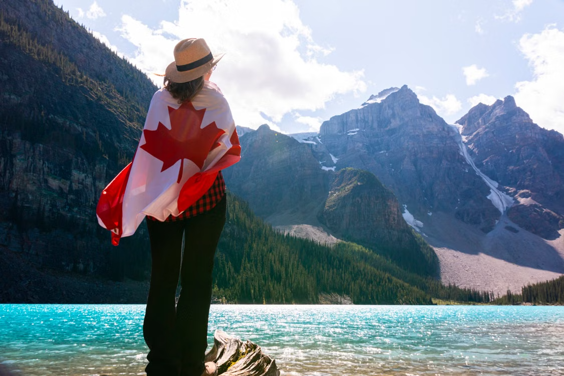 A woman wrapped in a Canadian flag overlooking a turquoise mountain lake